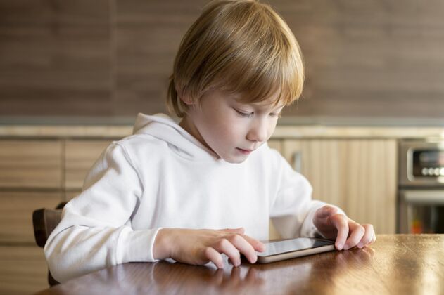 智能手机小男孩在桌旁使用智能手机的前视图科技娱乐孩子