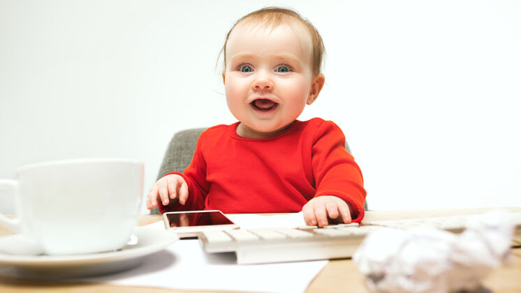 教育小女婴坐在白色工作室里 用现代电脑或笔记本电脑的键盘可爱婴儿年轻