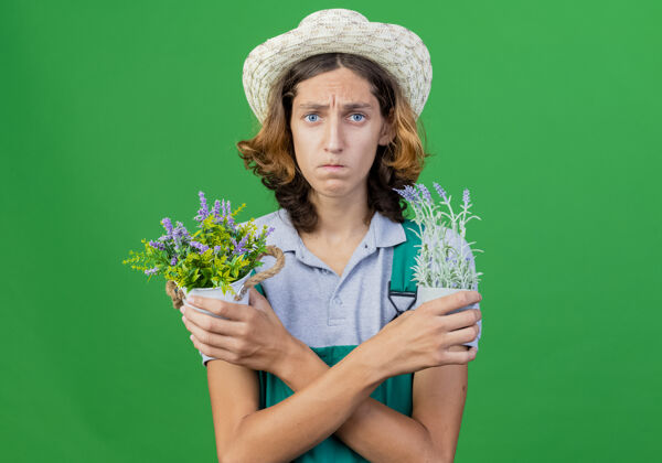 连身衣年轻的园丁 穿着连体衣 戴着帽子 手里拿着盆栽植物 表情悲伤植物年轻帽子
