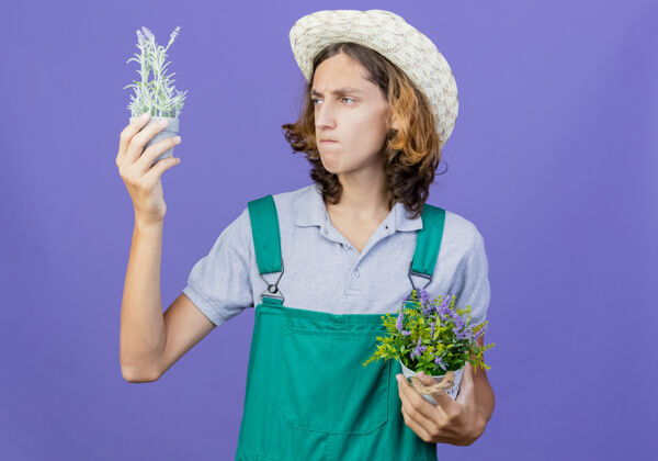 尝试年轻的园丁 穿着连体衣 戴着帽子 手里拿着盆栽植物选择锅穿