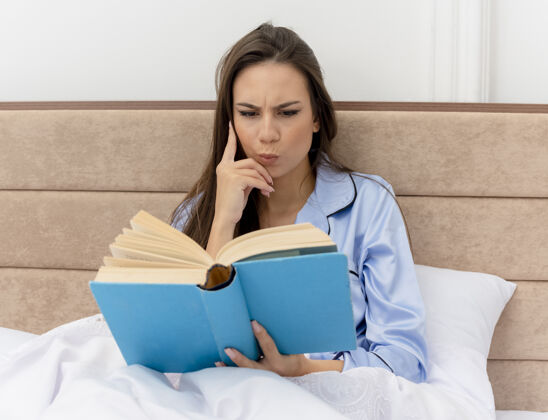女人穿着蓝色睡衣躺在床上的年轻漂亮女人读书坐着严肃