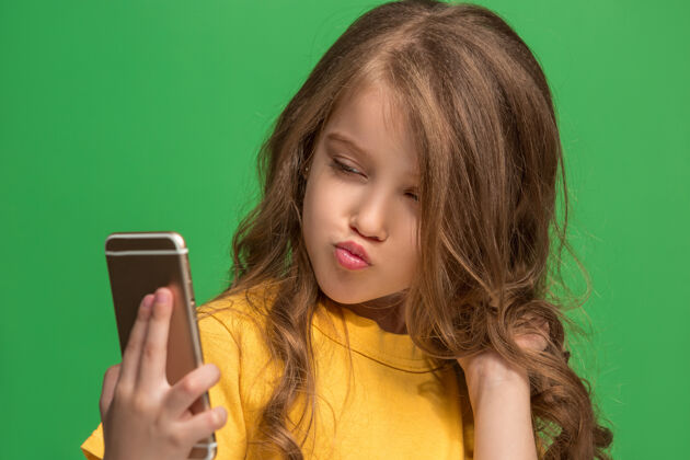 模特快乐的少女站着 微笑着用手机在时尚的绿色工作室青少年女士肖像