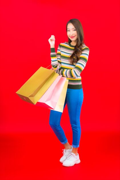 支付在红墙上画一幅美丽的亚洲年轻女子 带着五颜六色的购物袋互联网销售微笑