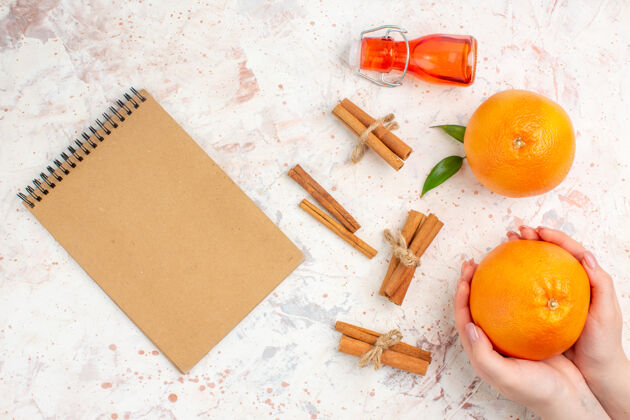 肉桂顶视图新鲜橘子肉桂棒橘子在女性手瓶笔记本上明亮的表面鲜橙抹刀甜瓜