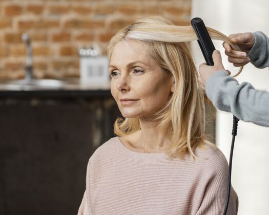 发型成熟的女人在家里由美发师把头发理直美容院直发器发型师