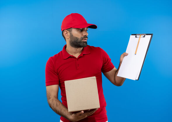 显示留着胡须的送货员穿着红色制服 拿着帽子的盒子 在蓝色的墙上放着一个空白页的剪贴板站着帽子胡子