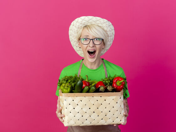年轻一位年轻的园丁 围着围裙 戴着帽子 手里拿着装满蔬菜的箱子板条箱帽子短