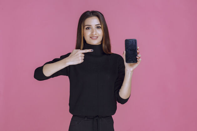姿势穿着黑色毛衣的女人拿着一部智能手机指着它客户年轻智能