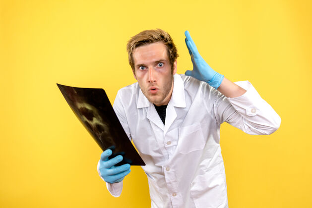 实验室外套正面图：男医生拿着黄色背景的x光片做医疗卫生手术视图持有实验室
