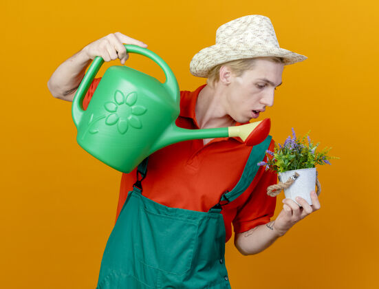 连身衣年轻的园丁穿着连体衣戴着帽子拿着浇水罐植物浇水锅