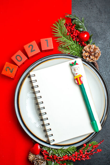 分针新年背景立面图 餐盘上有螺旋笔记本 装饰配件杉木树枝 黑色桌子上有红色餐巾上的数字餐巾视图数字