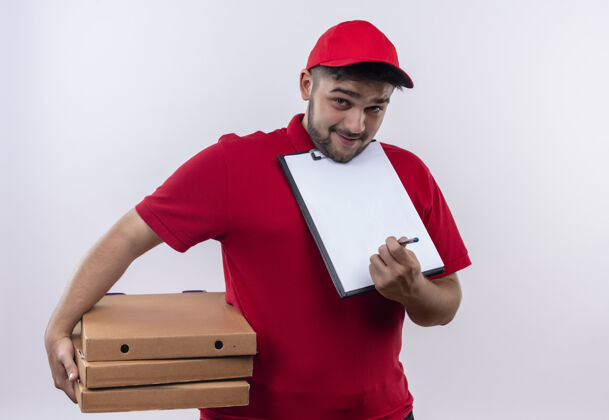 剪贴板年轻的送货员穿着红色制服 戴着帽子 手里拿着披萨盒 上面有空白页的剪贴板 要求签名红色询问年轻人