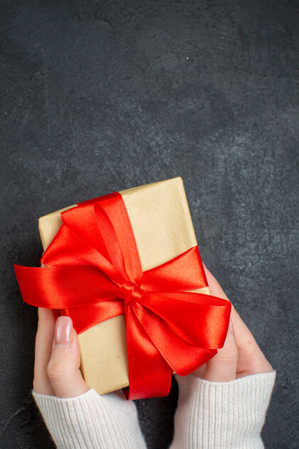 蝴蝶结手持精美礼品的垂直视图 黑色背景上有蝴蝶结形状的缎带圣诞蝴蝶结美丽的礼物