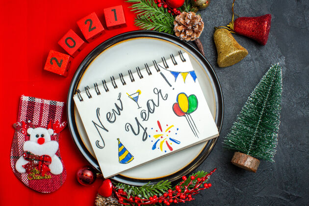 地球仪新年背景的顶视图与餐盘装饰配件杉木枝和数字在一个红色餐巾旁边的圣诞树在一个黑色的桌子上视图游戏设备顶部