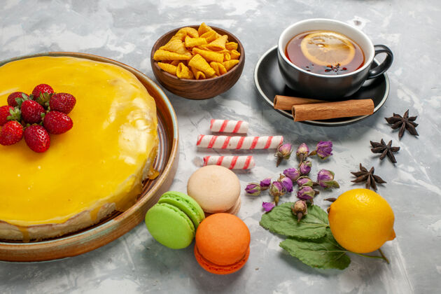 前面前视图黄色蛋糕和麦卡龙和浅白色表面上的一杯茶柑橘一餐饼干