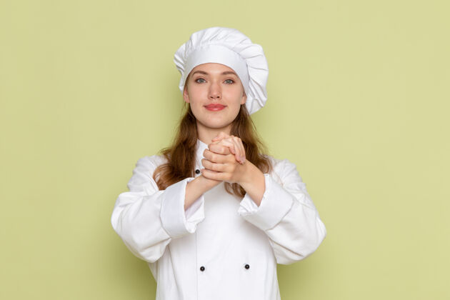 女身着白色厨师服的女厨师在浅绿色墙上微笑着摆姿势的正面图帽子摆姿势灯光