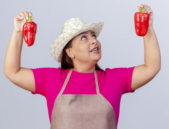 铃铛穿着围裙 戴着帽子的中年园丁妇女 展示着新鲜的红甜椒 微笑着看着它们站在白色的背景上女人花园看