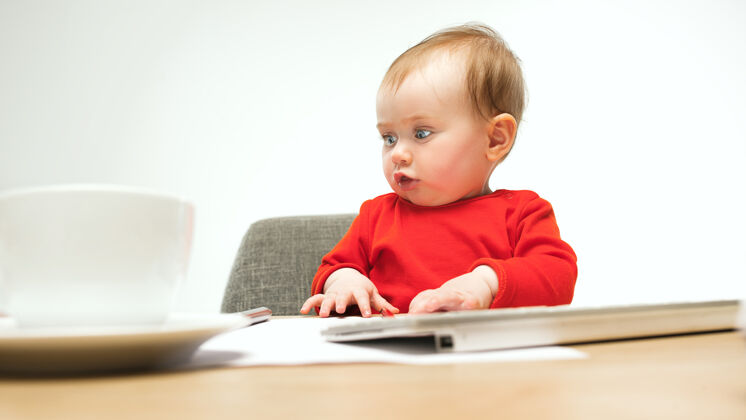 键盘快乐的小女婴坐在一个白色的工作室里 用现代电脑或笔记本电脑的键盘幼儿欢呼电脑