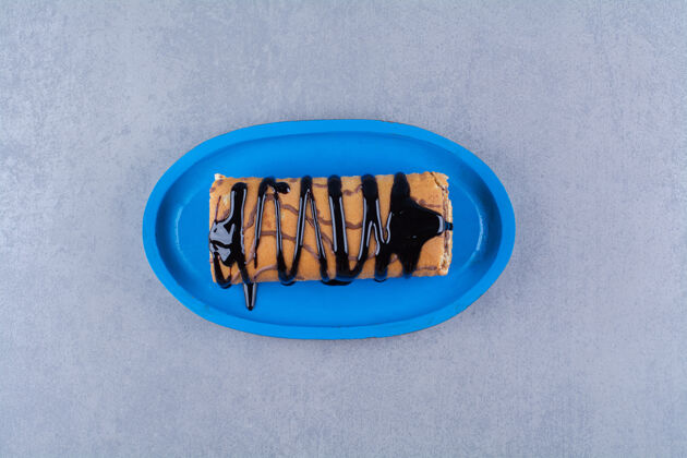 可食用一块蓝色的木板 上面是巧克力糖浆和奶油做成的美味甜面包卷美味吃烘焙