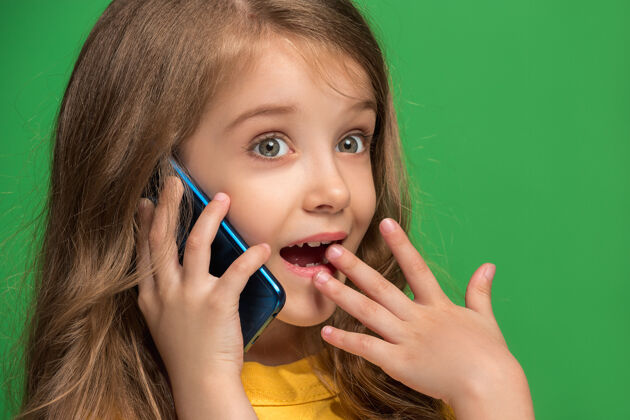面部快乐的少女站着 微笑着用手机在时尚的绿色工作室女性电话模特
