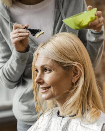 女性成熟的女人在家里被理发师染发美容师发型师垂直