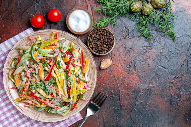 芽顶视图蔬菜沙拉放在盘子上桌布叉上盐和黑胡椒西红柿松枝放在深红色桌子上自由空间盘子西红柿午餐