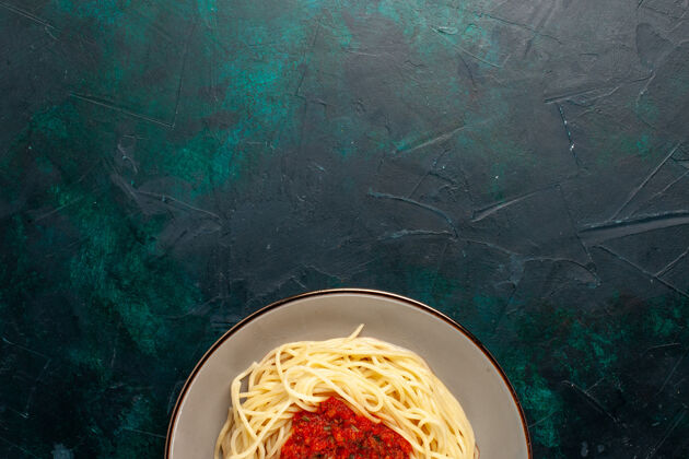 西红柿俯视图：深蓝色表面上有肉末和番茄酱的熟意大利面食意大利面意大利面顶部
