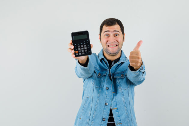 男人年轻人拿着计算器 在t恤衫 夹克衫上竖起大拇指 看上去很开心显示向上商人