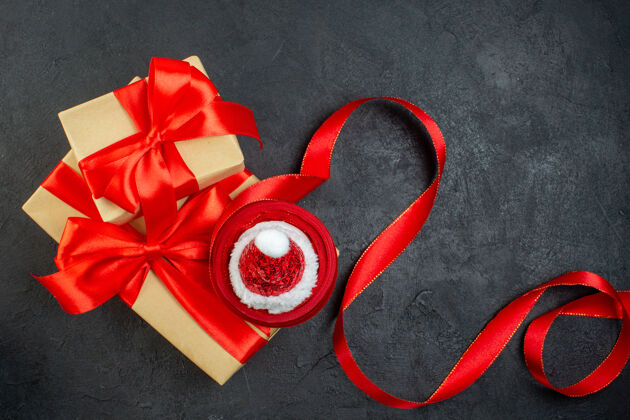 玫瑰俯瞰美丽的礼物与红丝带和圣诞老人帽子在黑暗的桌子上蝴蝶结圣诞节风景