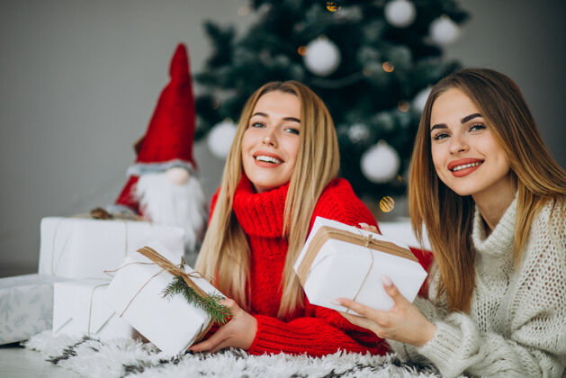 人两个女孩朋友在圣诞树旁拿着圣诞礼物传统圣诞树节日