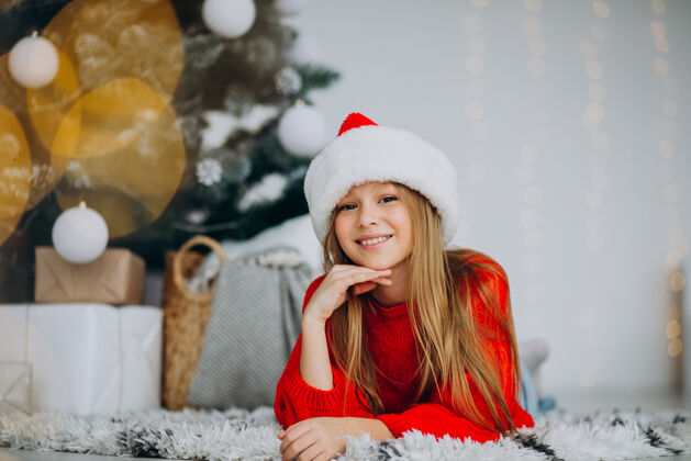 快乐女孩圣诞树下戴圣诞帽的漂亮女孩人年轻欢呼