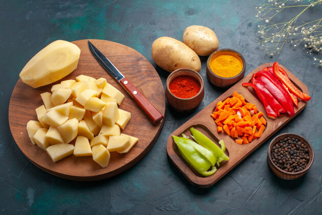 蔬菜半俯视图：在深蓝色的表面上切上带调味料的新鲜土豆片和辣椒片水果口味切片