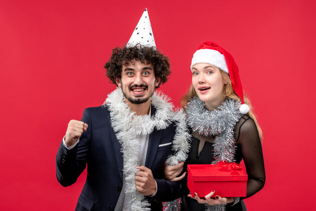 服装红桌圣诞爱情派对上 年轻夫妇拿着新年礼物的正面图年轻夫妇书桌成人