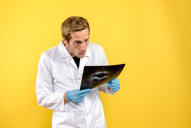 学者前视图男性医生检查头骨x光黄色背景医学手术covid-外科成人X光