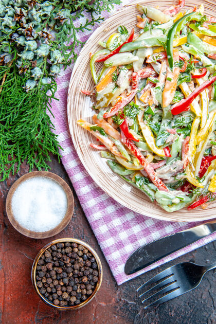 肉顶视图蔬菜沙拉在盘子上桌布叉子和刀子上盐和黑胡椒松枝在暗红色的桌子上绿色顶食物