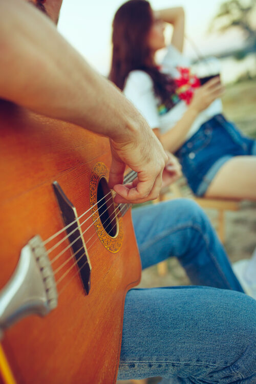 爱情一对情侣坐在沙滩上休息 在河边的夏日里弹吉他在一起啤酒度假