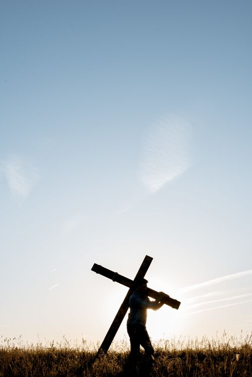 冒险在蓝天下的草地上 一只雄性手持手工制作的木制十字架的垂直镜头教堂健康宗教