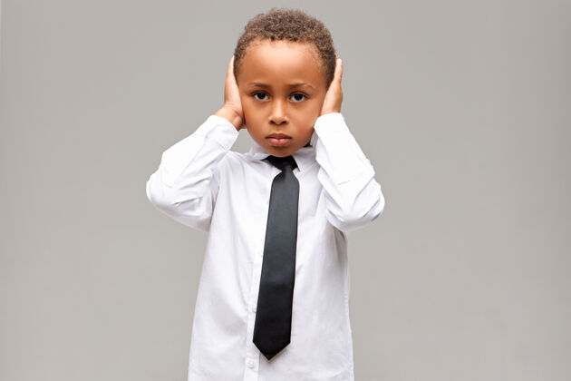 童年穿着校服的非洲裔美国男孩的悲伤和不快乐的画像 他沮丧的面部表情 用手捂住耳朵 无法忍受父母的争斗肢体语言 反应和感情领带年轻情感