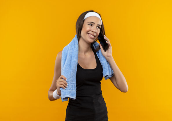 漂亮微笑的年轻漂亮的运动女孩戴着头带和手环与毛巾在她的脖子上橙色空间年轻头带毛巾