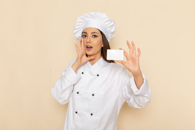 工人身穿白色厨师服的年轻女厨师的正面图 在浅白的墙上举着白色的牌子烹饪举行人