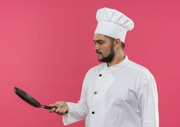 厨师年轻的男厨师身着厨师制服 手拿煎锅看着粉红色的空间隔离年轻男煎