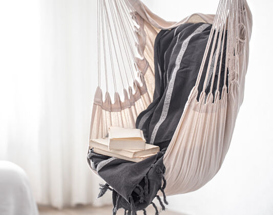 斯堪的纳维亚波西米亚风格的吊床椅和一堆书这是一个在家放松的舒适的地方房间椅子文学