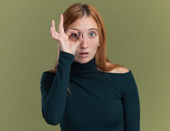 橄榄令人印象深刻的年轻红发姜女孩雀斑通过手指隔离在橄榄绿的墙壁与复制空间年轻红发手指