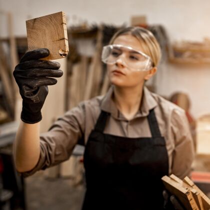 木工女木匠戴着眼镜看着一块木头职业资格职业工人