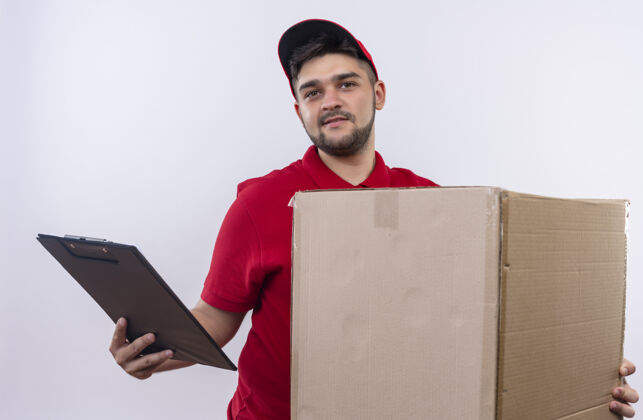红色年轻的送货员穿着红色制服 戴着帽子 手里拿着一个大盒子和一个剪贴板 脸上带着微笑 看上去很自信制服年轻微笑