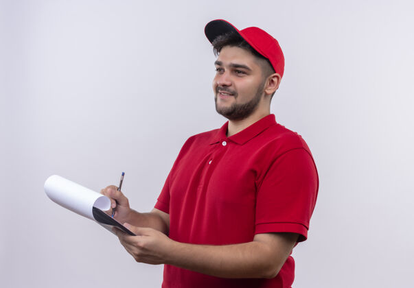 剪贴板年轻的送货员穿着红色制服 戴着帽子拿着剪贴板 空白的纸上写着微笑和自信站着男人自信