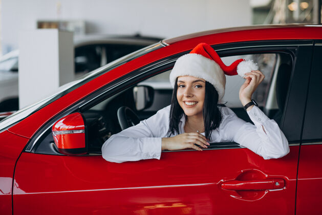 现代一个戴着圣诞帽的女人坐在汽车陈列室里的红色汽车旁边快乐惊喜新的