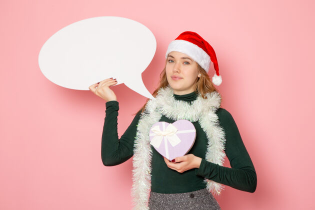 帽子正面图年轻女性手持白色大招牌 在粉色墙上呈现模特圣诞新年的色彩情感幸福情感色彩