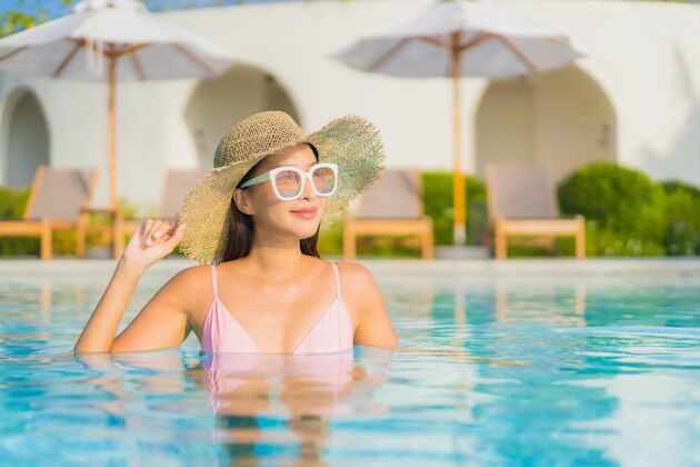 亚洲肖像美丽的亚洲年轻女子放松休闲围绕室外游泳池与海水帽子酒店