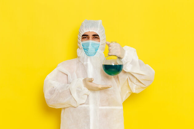 科学身穿特殊防护服的男性科学工作者的正面图 黄色墙壁上有面罩固定瓶科学外套危险
